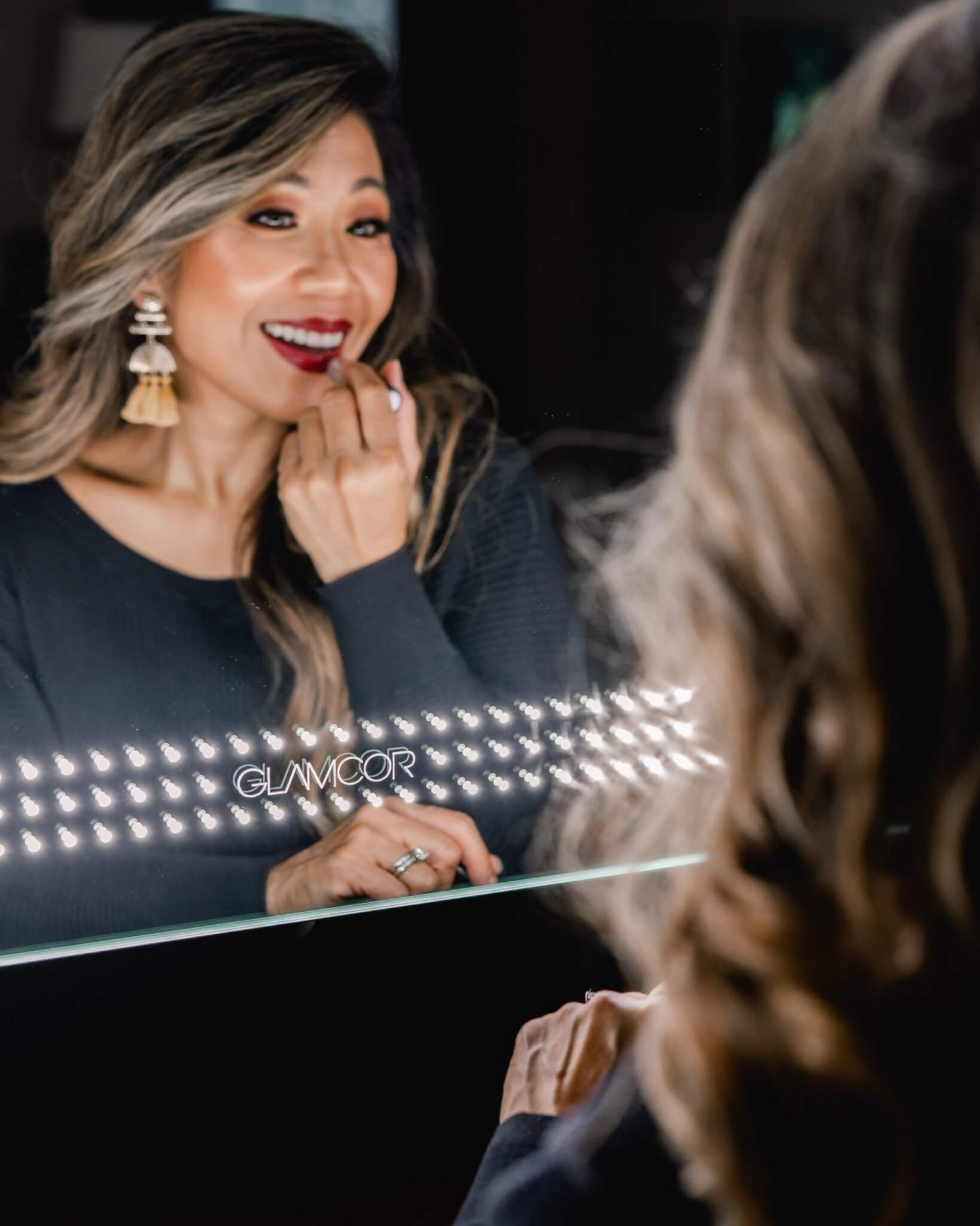 woman standing in front of glamcor socialite mirror smiling and applying red lipstick