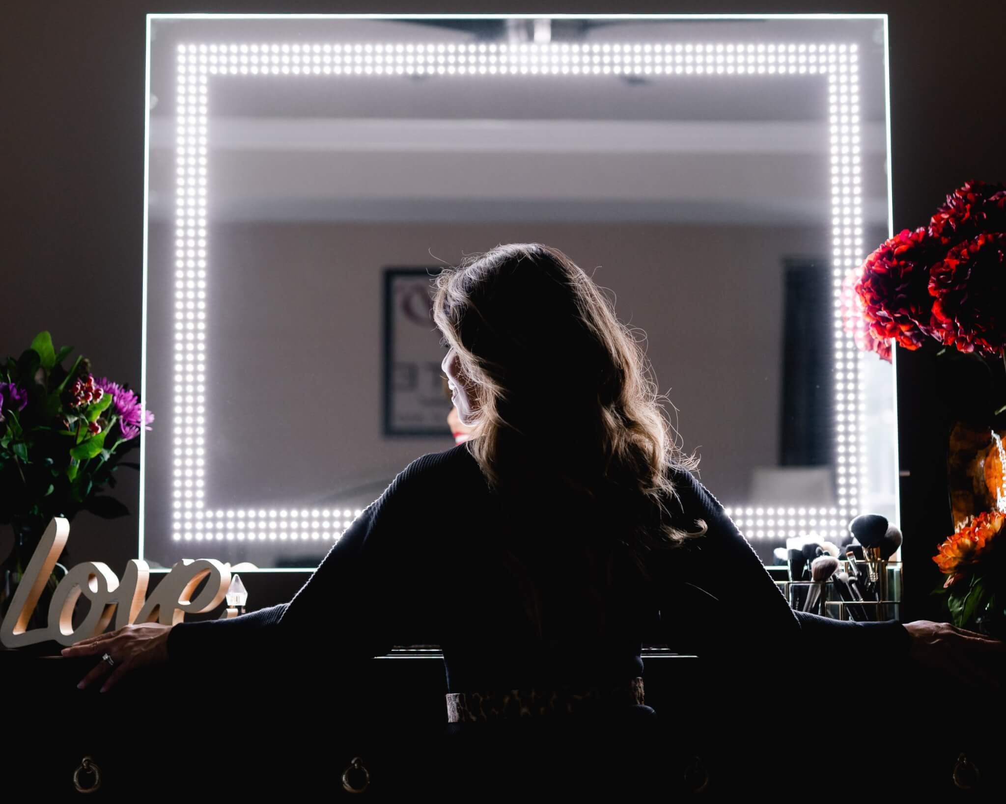 smiling woman facing sideways standing in front of glamcor socialite mirror with led lights on the brightest setting