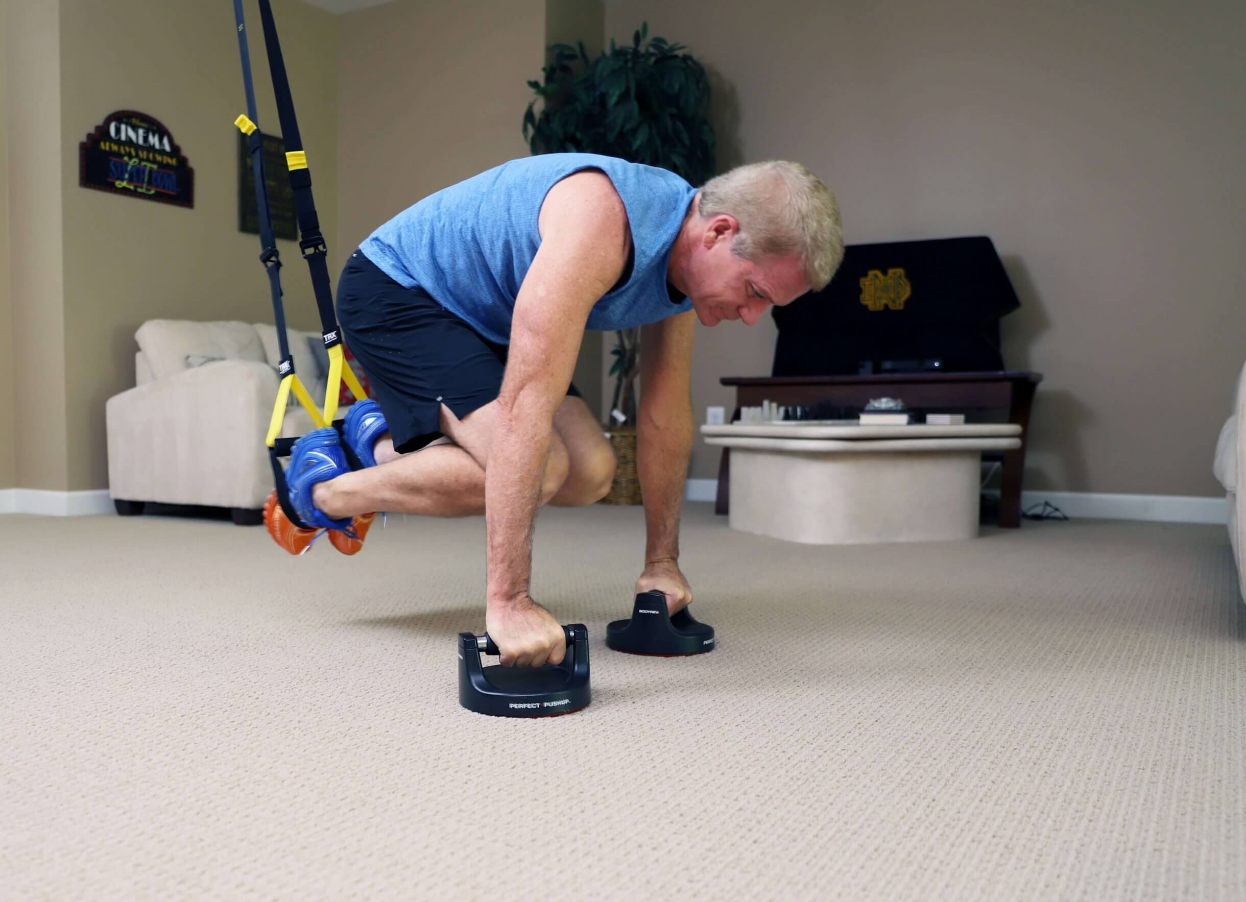 man in atomic pushup with feet in TRX cradle and legs inward, hands in pushup paddle