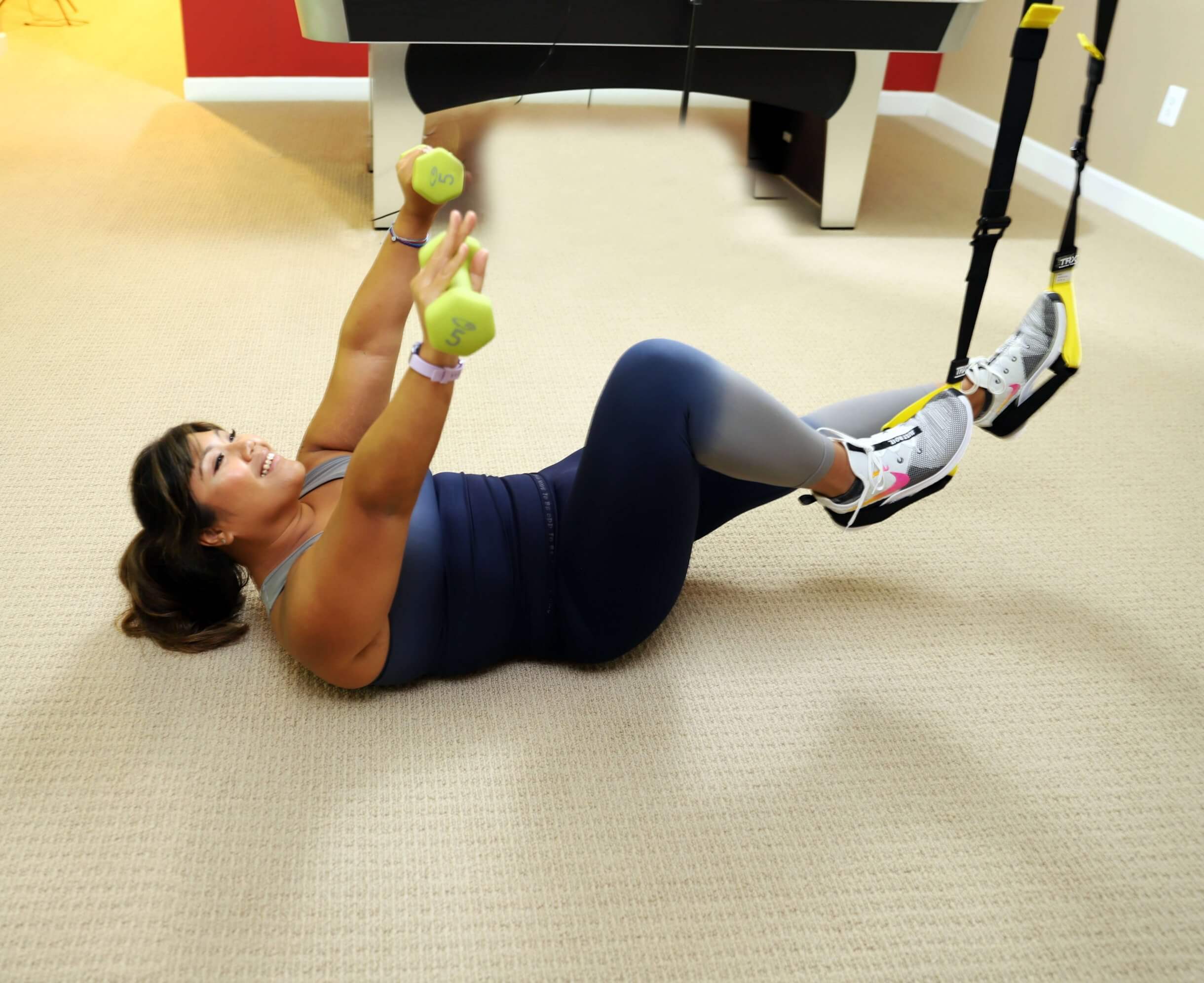woman doing trx ab exercises with shoulder up raising hand with weights while feet cradled in TRX