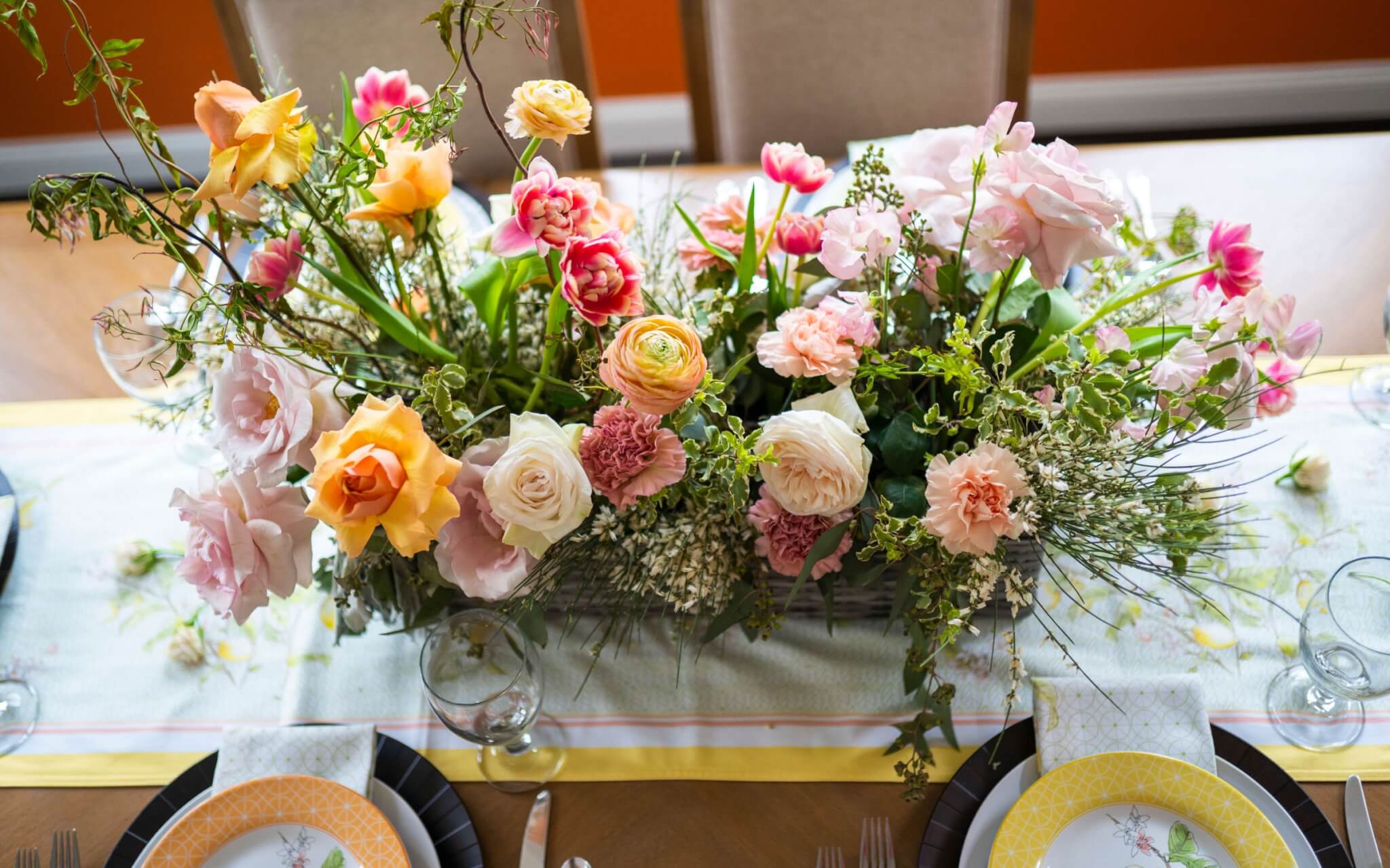 floral centerpiece in spring pink and orange blooms in roses, tulips, ranunculus, carnations, and sweet pea