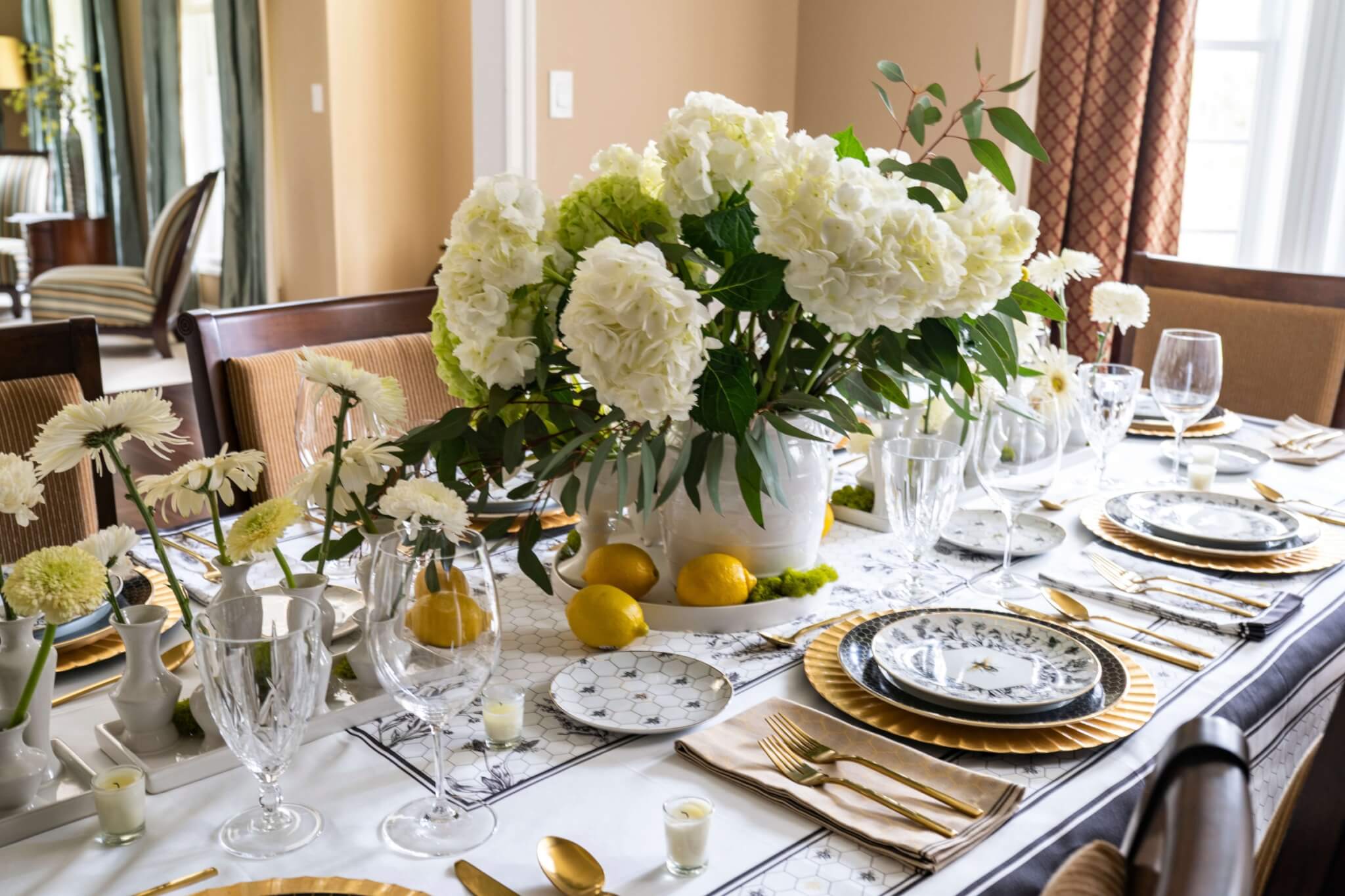 bee inspired dinnerware place setting in black and gold colors.  Beautifully arranged in formal dining room with bountiful white hydrangeas and lemons 