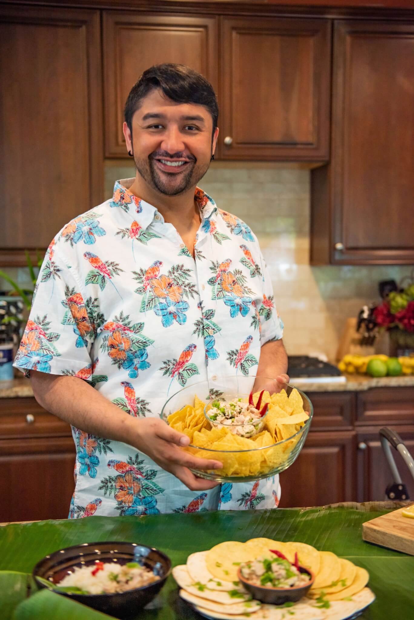 man from the Northern Marianas wearing a tropical shirt and holding up Chicken Kelaguen as a dip with tortilla chips