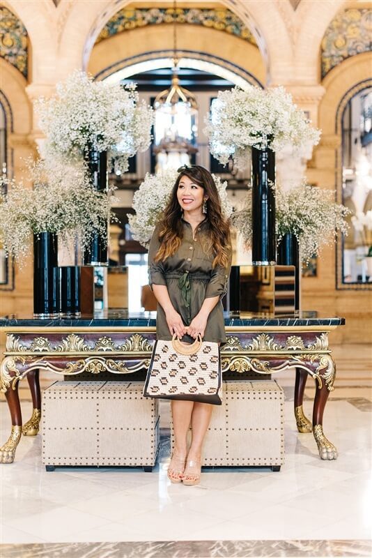 Predupre standing at the Hotel Alfonso XIII lobby wearing olive green romper with handbag