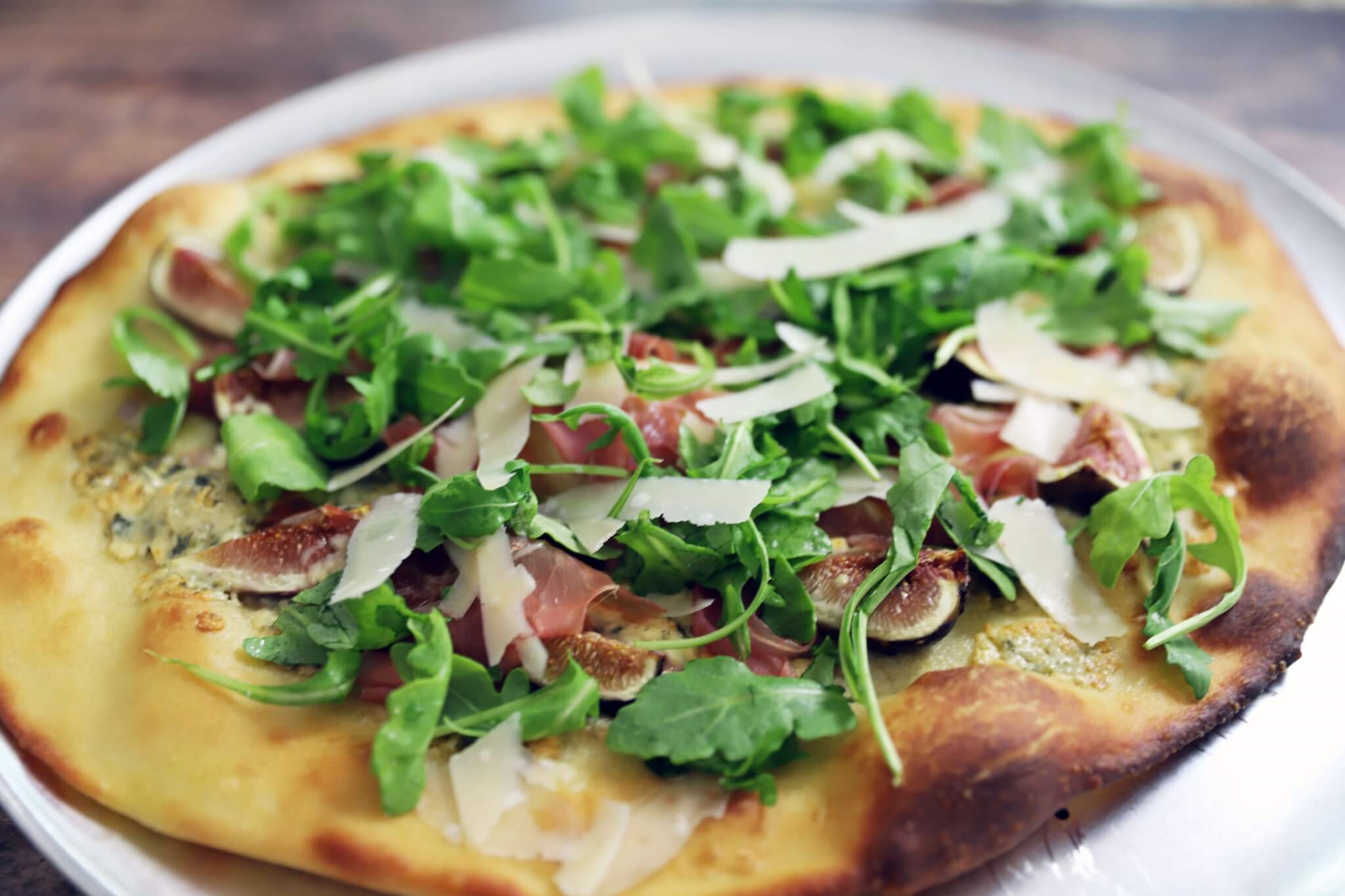 fig and prosciutto pizza with arugula salad and lemon vinaigrette, topped with shaved parmesan cheese