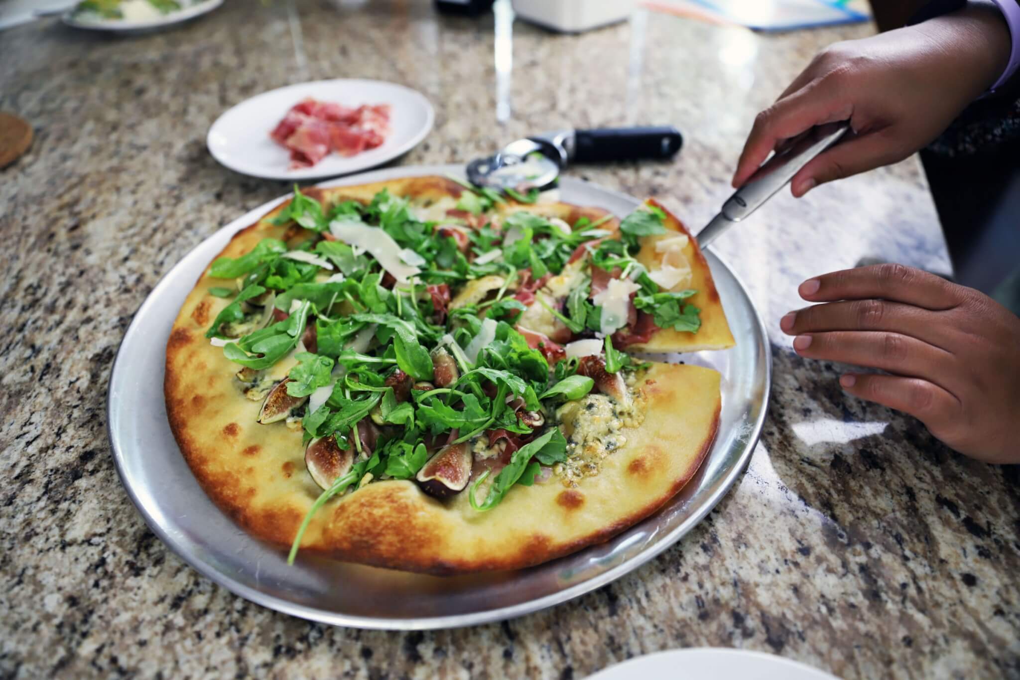 fig and prosciutto pizza with arugula salad and lemon vinaigrette, topped with shaved parmesan cheese