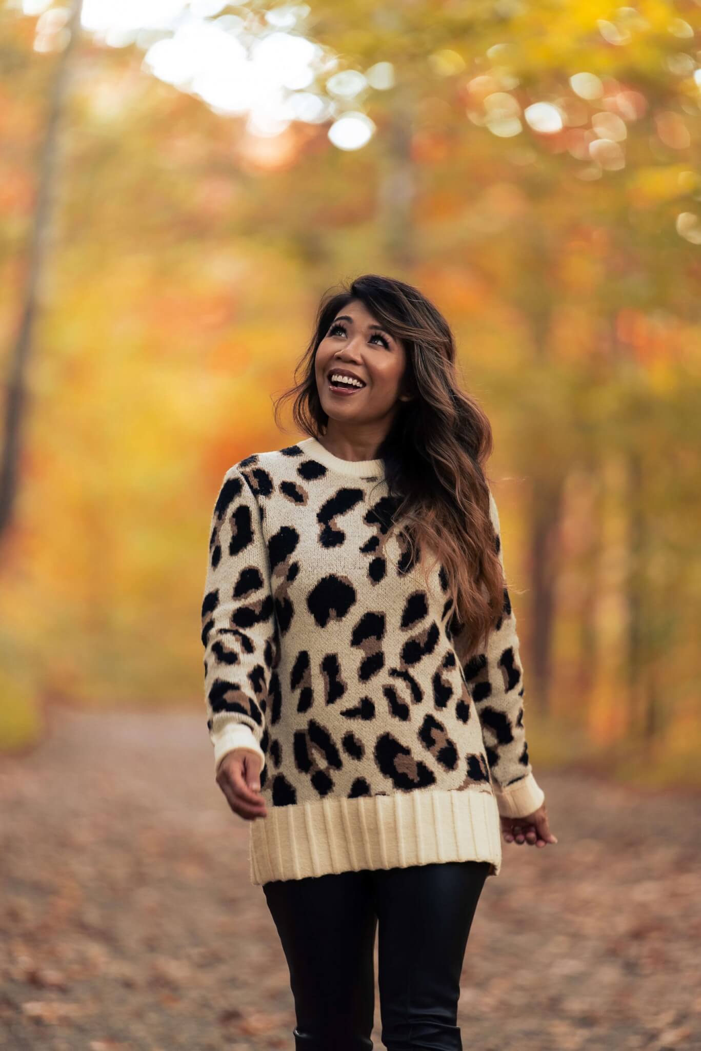 woman wearing leopard print sweater from Revolve as she walks through the forest during fall
