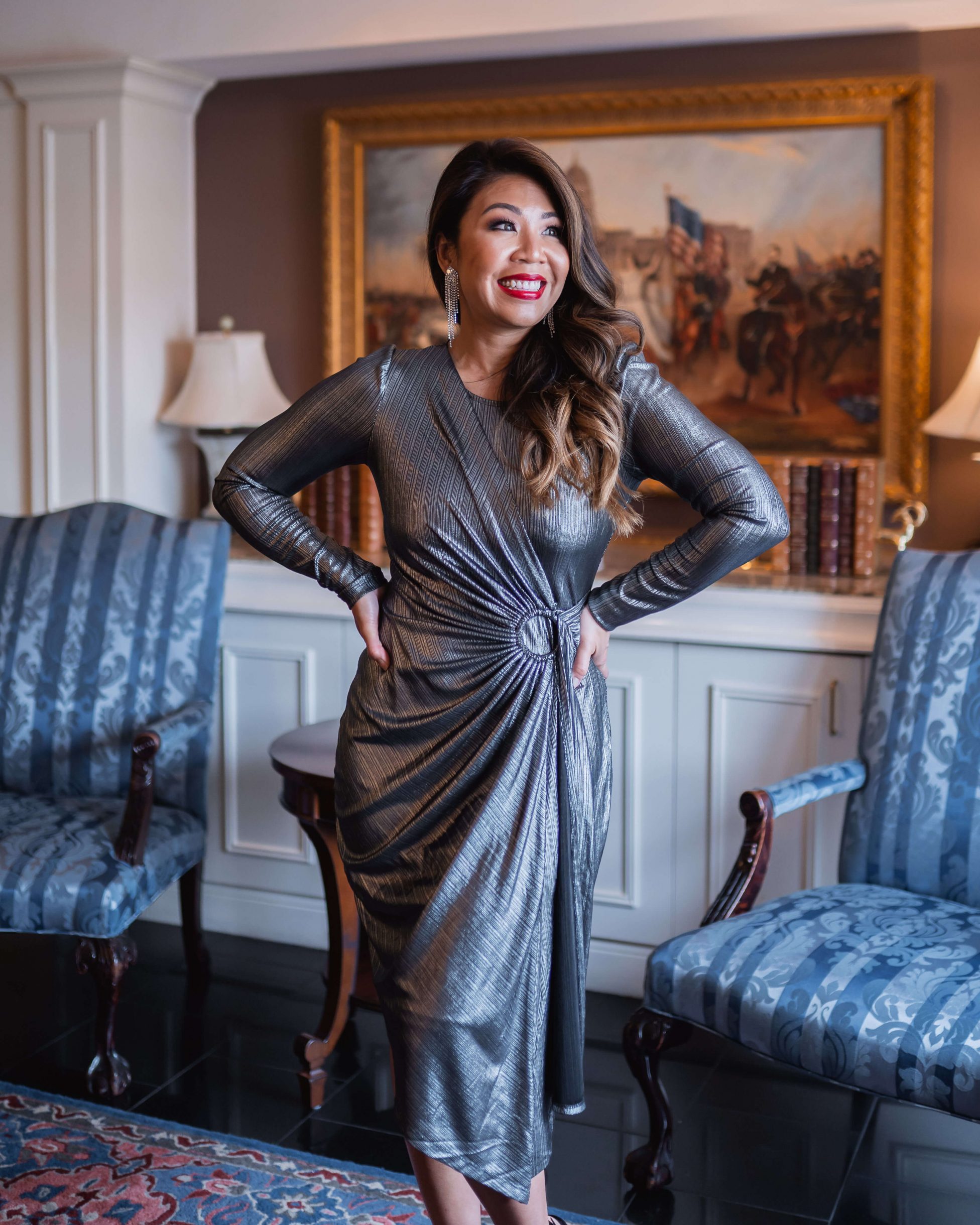 woman standing with both hands on her waist, looking to one side. she's wearing a metallic silver midi dress with her hair styled with classic Hollywood Waves.