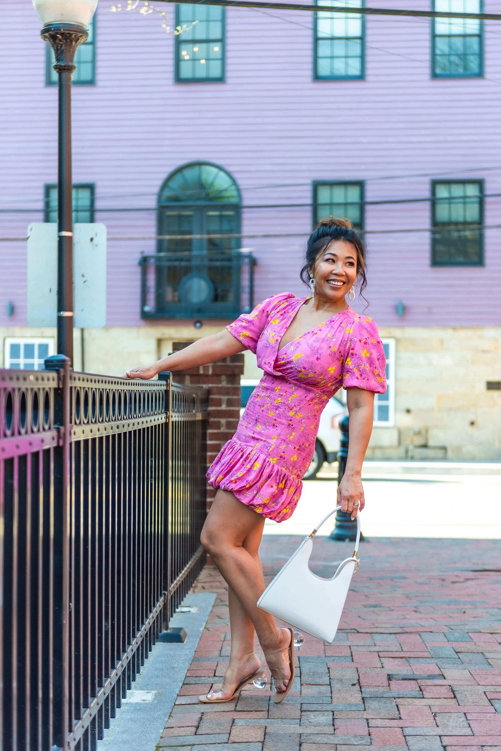 lady wearing a hot pink floral fitted dress with a balloon hem and heels and white bag.